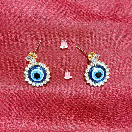 Close-up of gold evil eye earrings with a crystal halo design on a vibrant red fabric background.