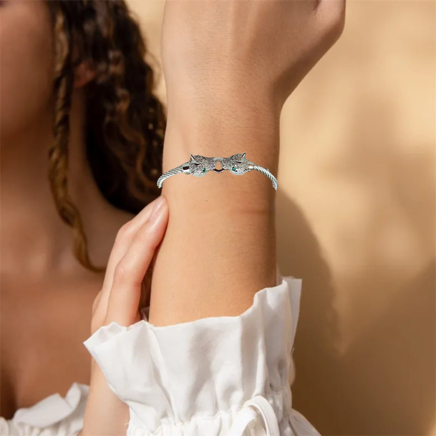 A silver cuff bracelet featuring two detailed jaguar heads with emerald-green eyes