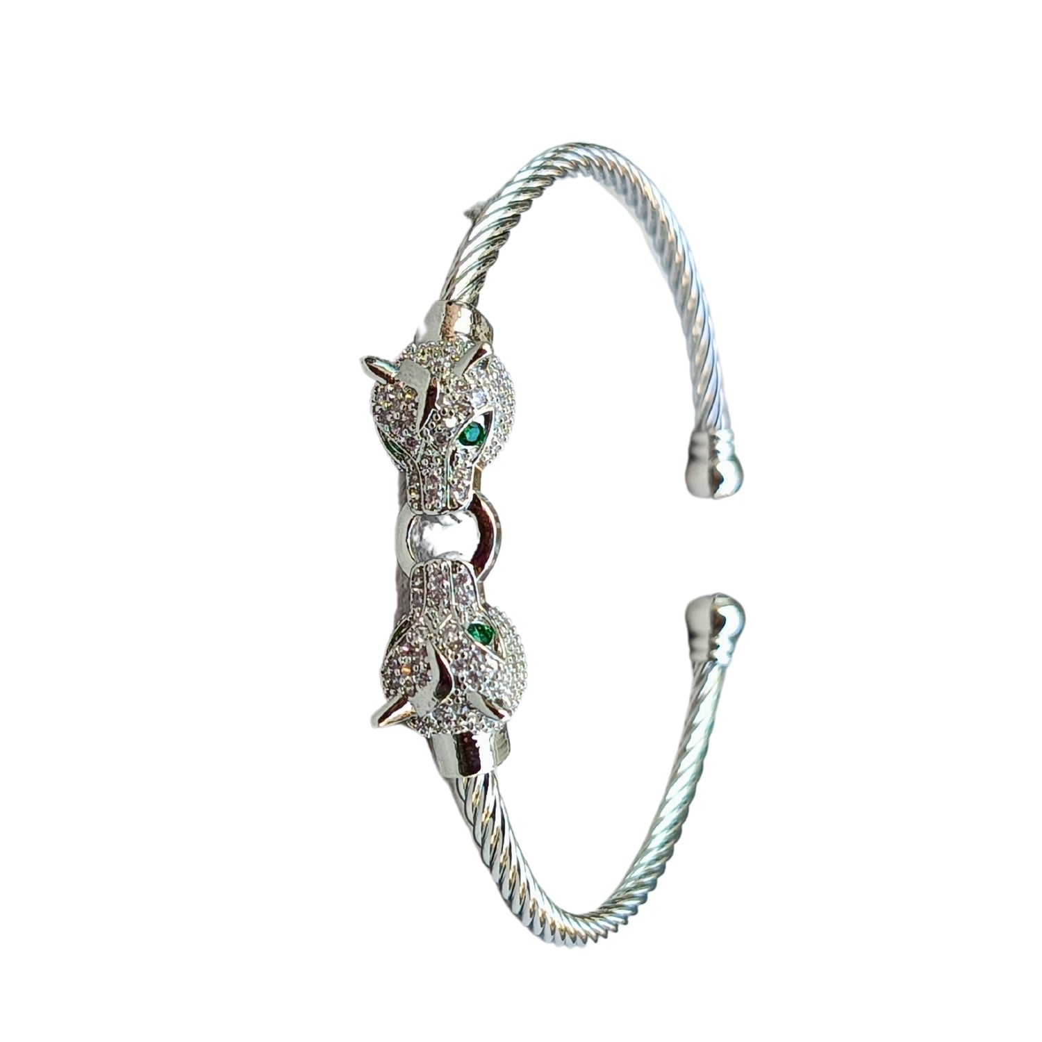 A silver cuff bracelet featuring two detailed jaguar heads with emerald-green eyes